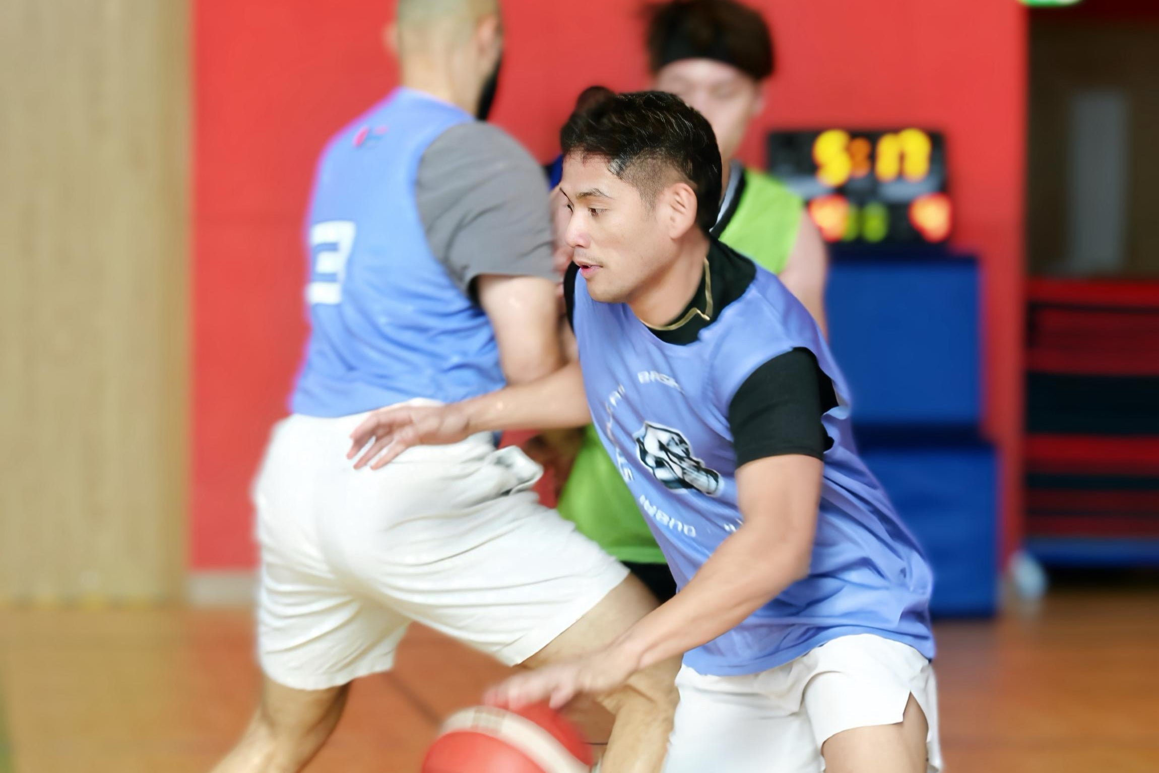 Two men playing basketball indoors with a red wall in the background, at Dubai Basketball Pickup Run Game.